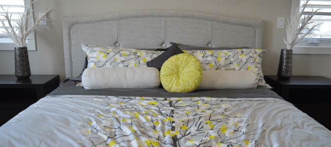 A bed with a gray comforter and yellow and white pillows