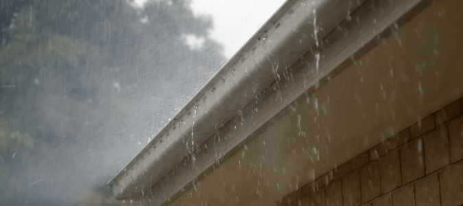 Water flowing over the top of a home's gutters due to a clogged downspout