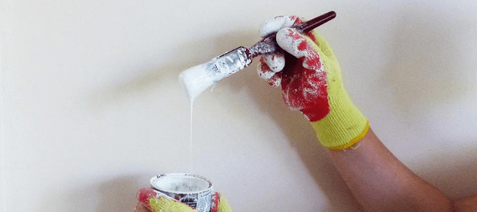 a homeowner wearing red and yellow painting gloves with a paintbrush in hand getting ready to paint trim without tape