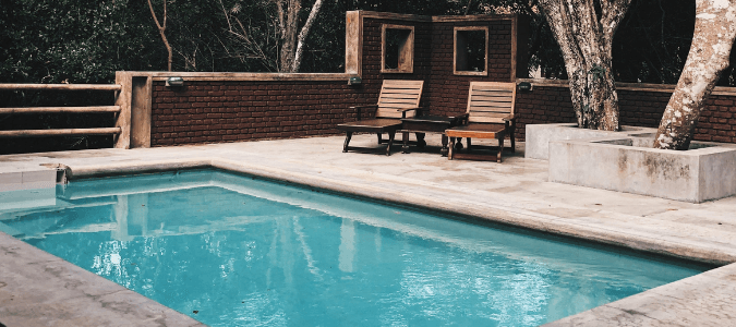 a pool at a home with two deck chairs and a retaining wall