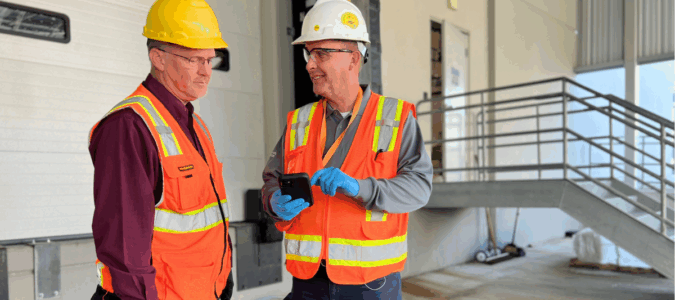 Two ABC team members are wearing hard hats and safety gear outside a commercial facility.